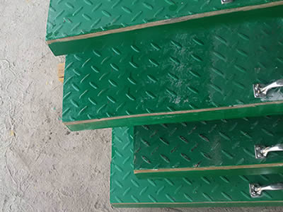 Four pieces of green color covered FRP gratings with metal handle on the ground.