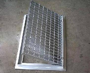 A hinged drainage trench box grate with serrated surface.