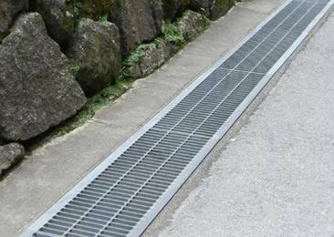 The side angled drainage trench grates are installed on the ground.
