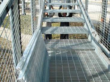 Two workers are installing welded steel grating stair treads.