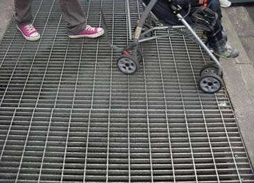 A woman pushing a baby carriage is passing the close mesh grating walkway.